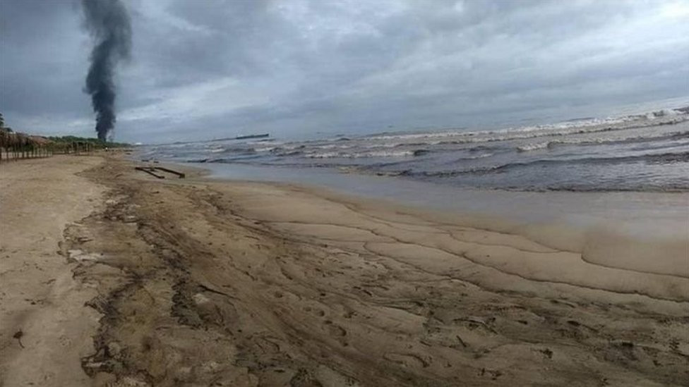 A beach with waves which appear dark with oil
