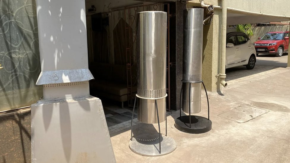 Tubular devices designed by Angad Daryani outside a building with parked cars in the background