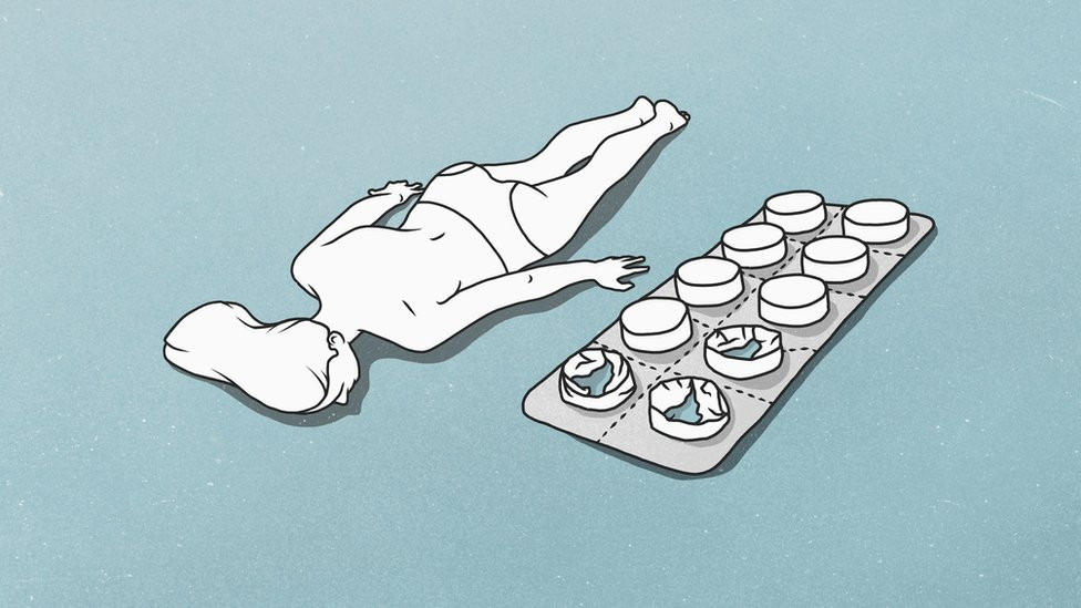 A female figure lying down next to a giant blister pack of tablets