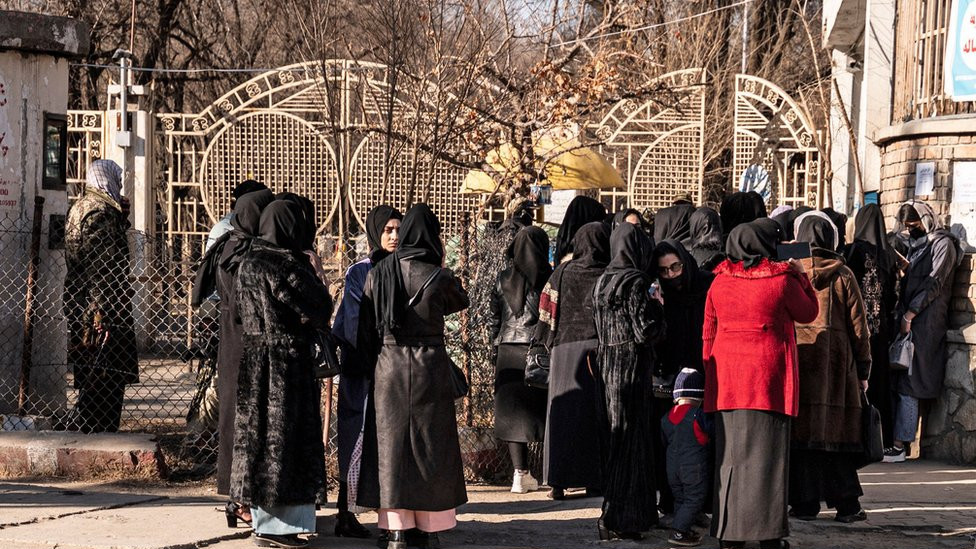 Afghan female university students stop by Taliban security personnel stand next to a university in Kabul on December 21, 2022.