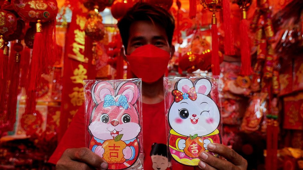 A man in Indonesia surrounded by Lunar New Year decorations holds gifts depicting rabbits