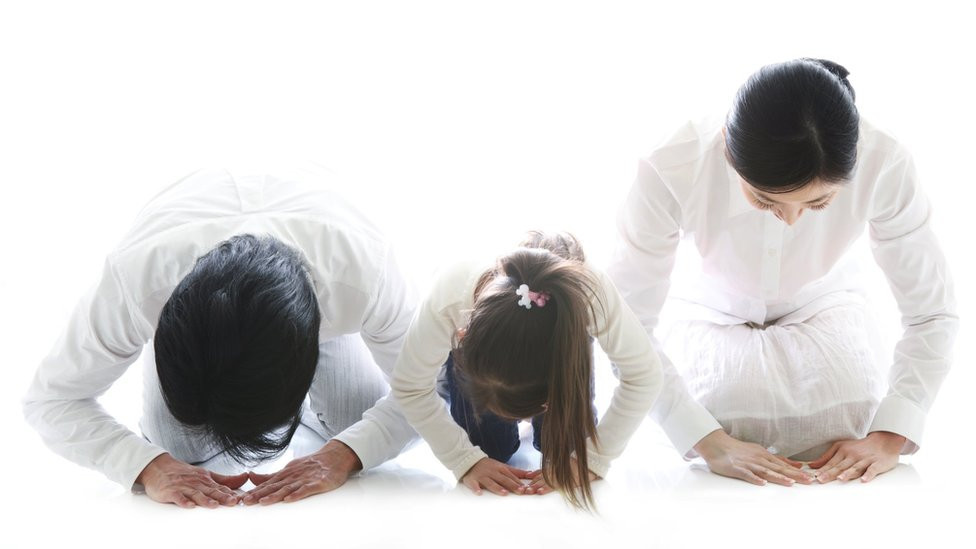 A father, daughter and mother wearing white, kneeling and bowing in a traditional manner