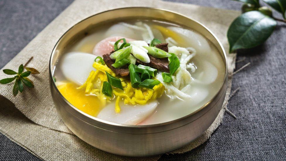 A bowl of rice cake soup, consisting of the brothp (guk) with thinly sliced rice cakes (tteok) - it is tradition to eat tteokguk on Lunar New Year's Day because it is believed to grant the consumer good luck for the year and gain a year of age. It is usually garnished with thin julienned cooked eggs, marinated meat, and gim