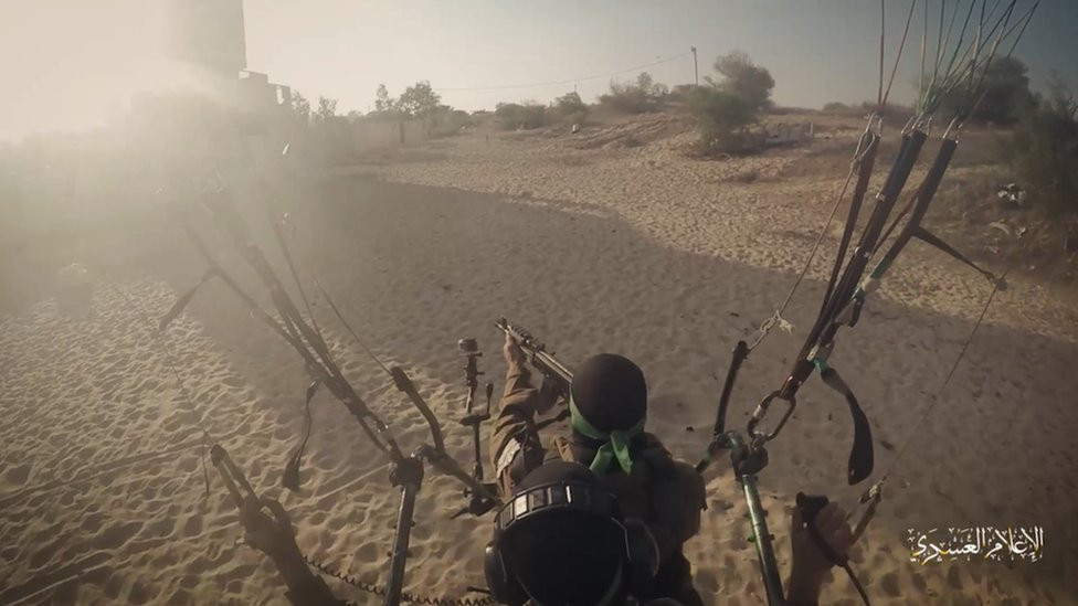 A Hamas fighter inside a cage carried by a parachute and pointing a gun