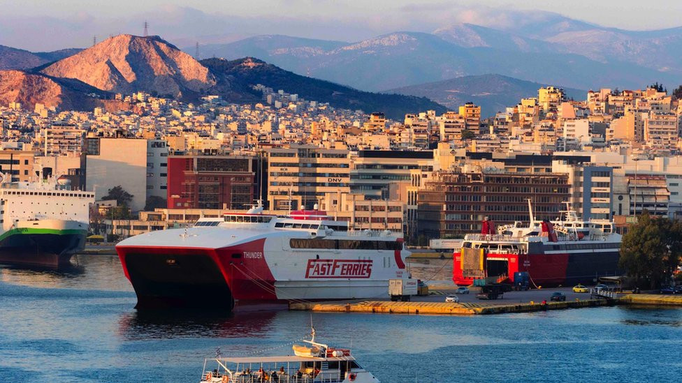 Panoramic view of Piraeus, Greece at sunset showing small and large ferries and mountains in the background