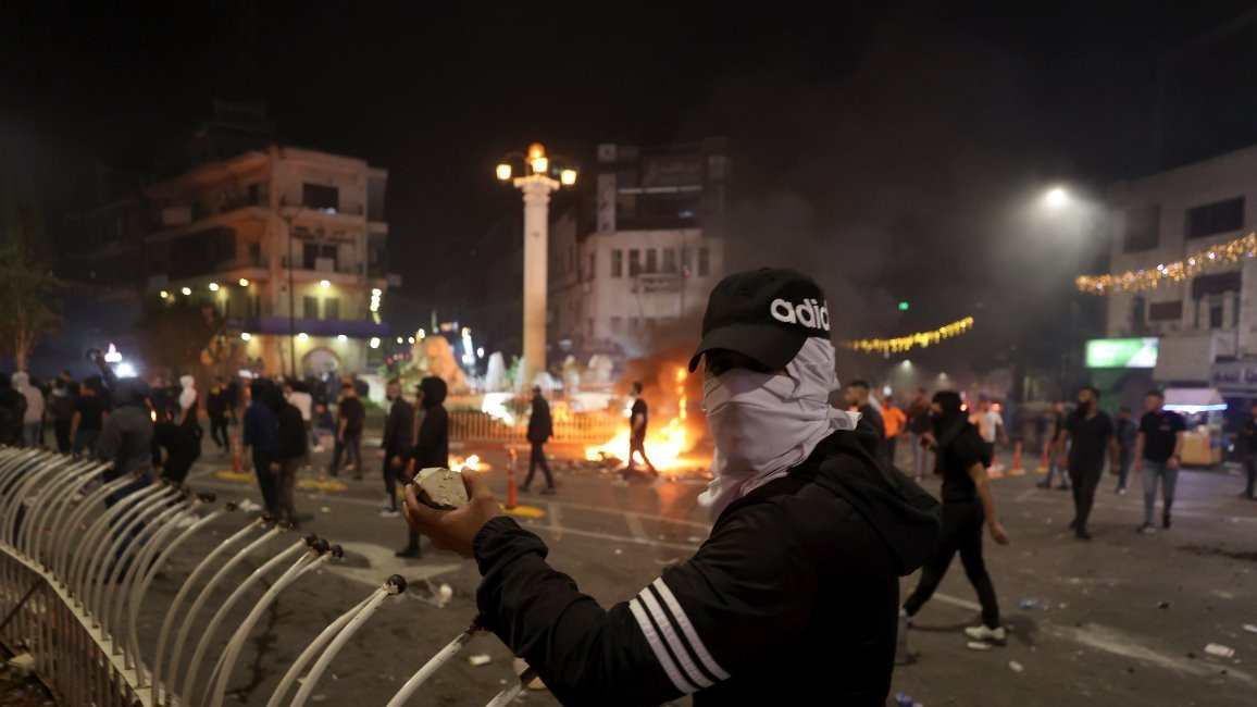 Masked protester holding rocks in front of a barricade and fires