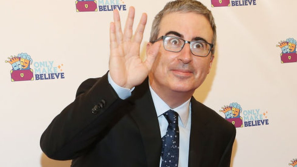 John Oliver pulling a funny face while waving