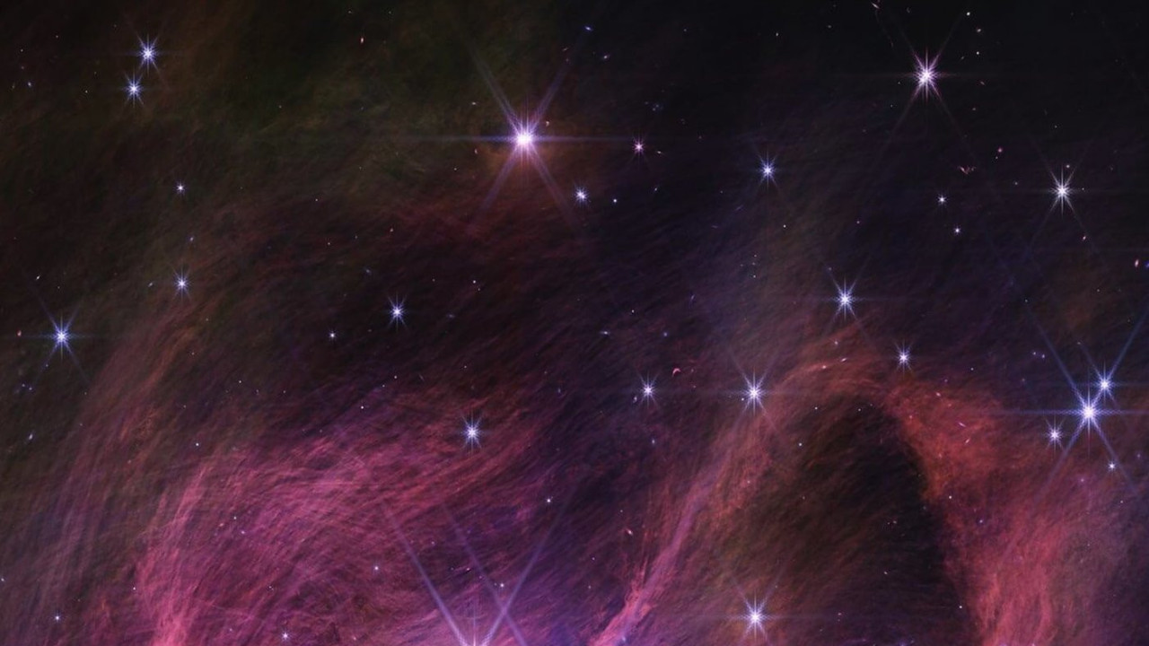 Orange and pink wisps of gas and dust stream between stars