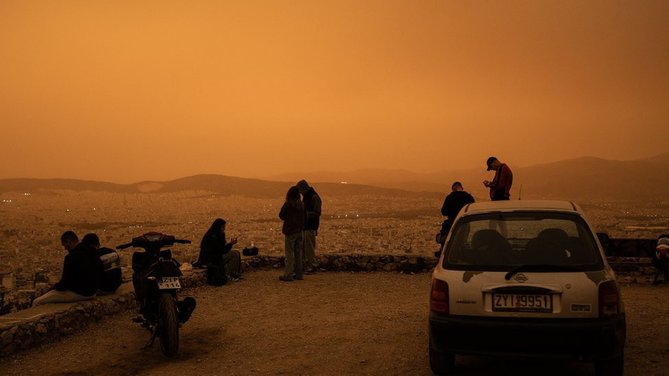 Ljudi sede na brdu Turkovunija sa pogledom na Atinu, dok južni vetrovi nose talase saharskog peska u grad, u Atini, 23. aprila 2024.