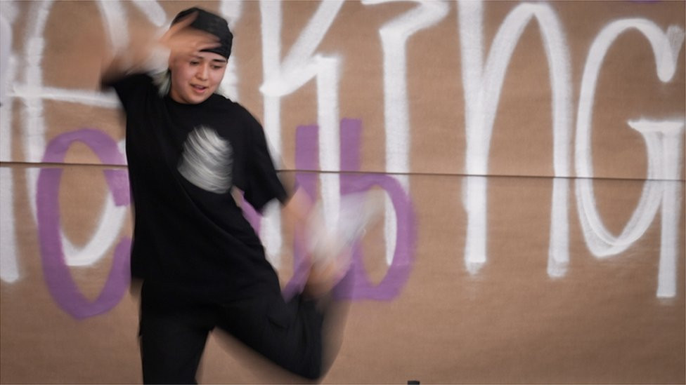 Manizha Talash breakdancing in front of a wall with graffiti on it