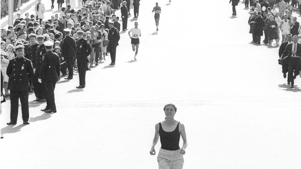 Bobbi Gibb runs alone with spectators watching her in the 1966 Boston Marathon