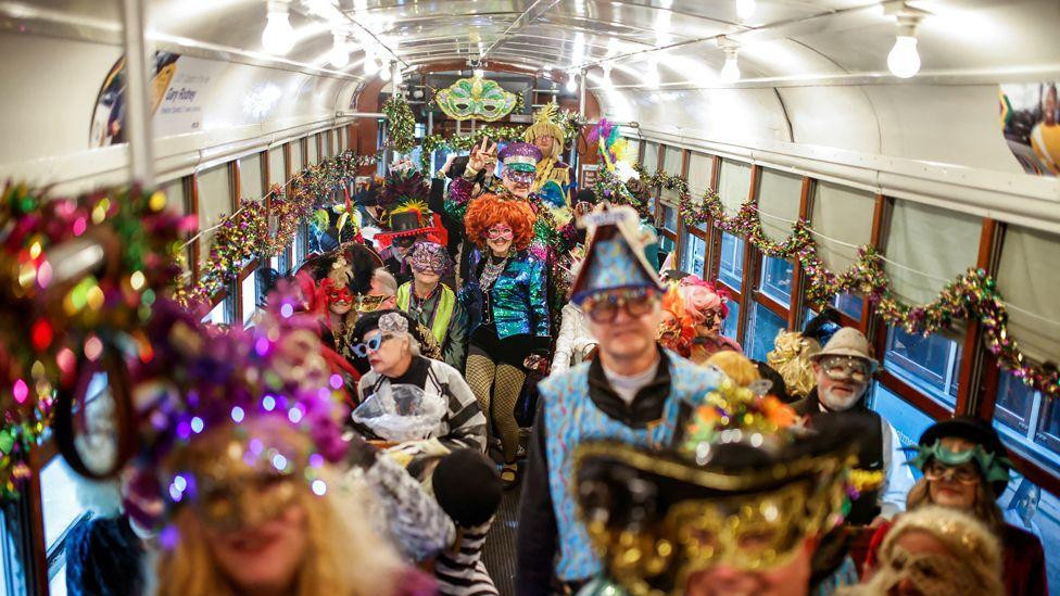 Ljudi sa maskama u kostimima, perikama i maskama u tramvaju tokom parade u Nju Orleansu 