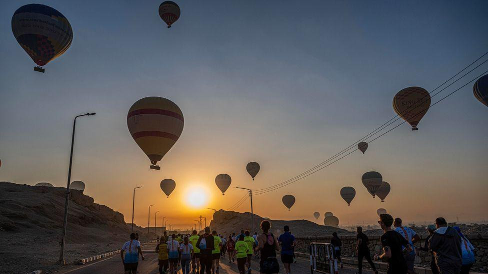 Izlazak sunca na nebu ispunjenom balonima na vruć vazduh dok ljudi trče na Egipatskom maratonu 