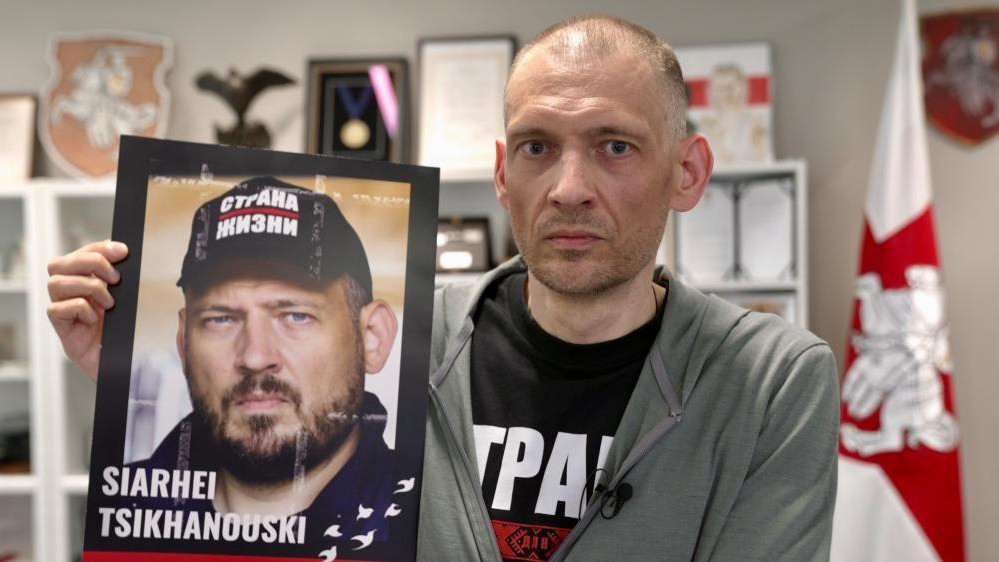 Sergej Tihanovski drži plakat sa vlastitom slikom da bi pokazao kako je izgledao pre nego što je uhapšen