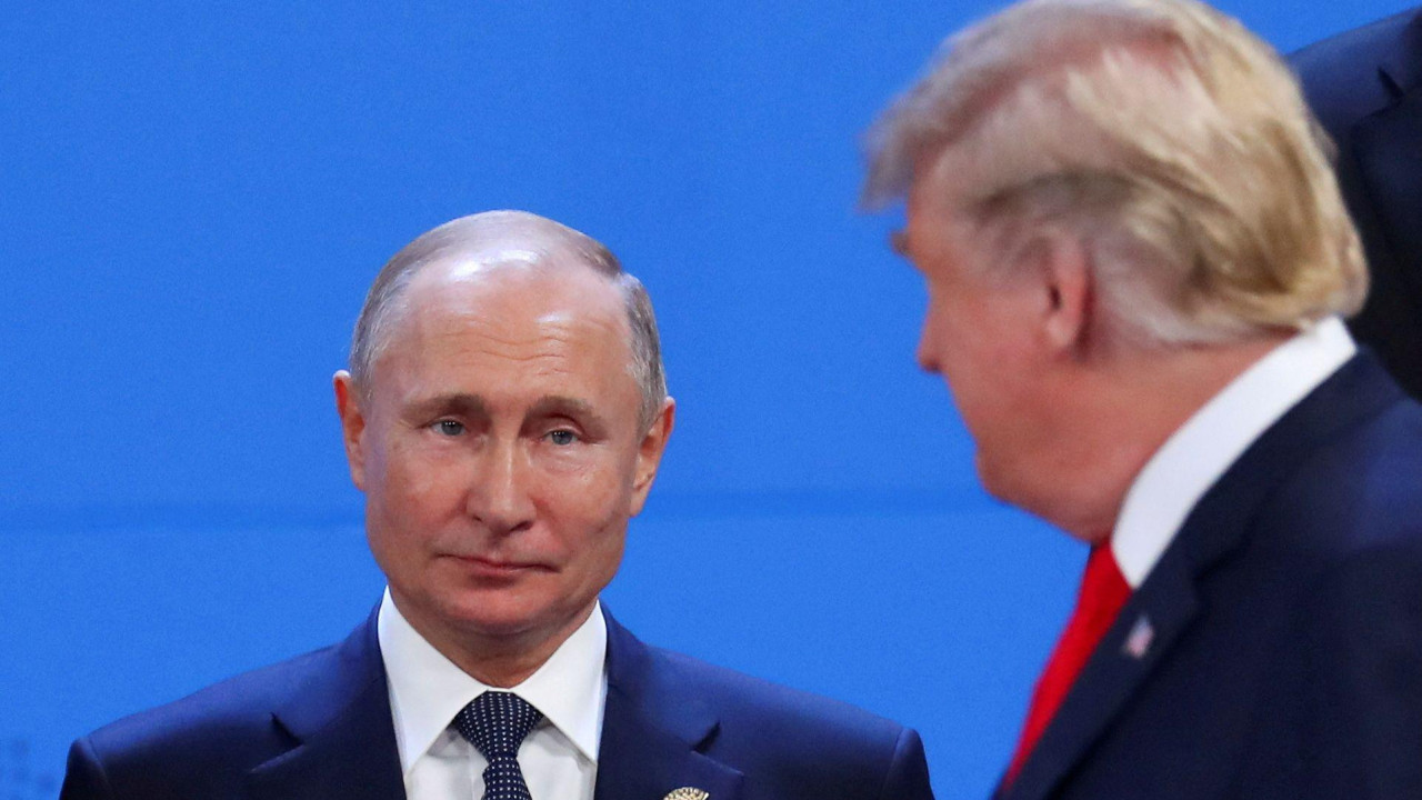 
                    Vladimir Putin, who has thinning grey hair and wears a navy suit, white shirt and navy polka dot tie, looks toward Donald Trump, who has blonde hair combed to the side an