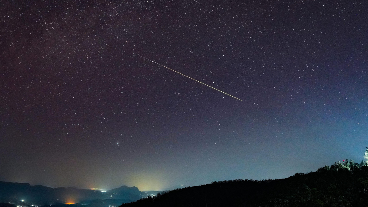 Veliki Perseid meteor dijagonalno prelazi zvezdano noćno nebo iznad Haputala, Šri Lanka - u prvom planu se vide tamna brda sa svetlima zgrada