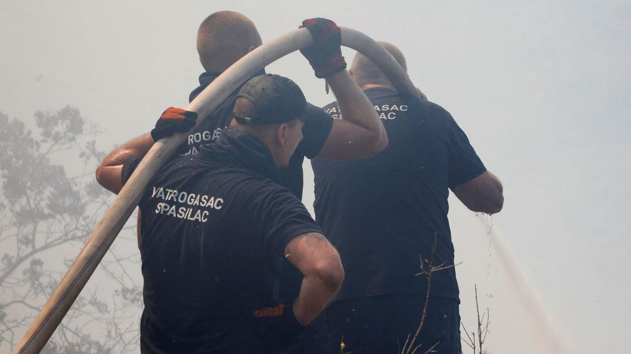 Trojica vatrogasaca drže crevo i pokušavaju da ugase vatru