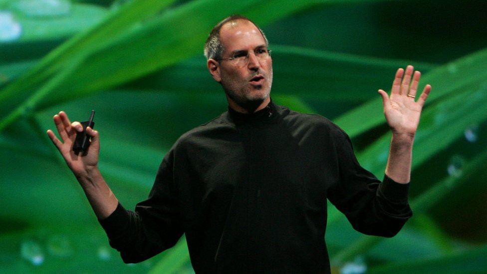 Steve Jobs standing in front of an image of leaves with water droplets